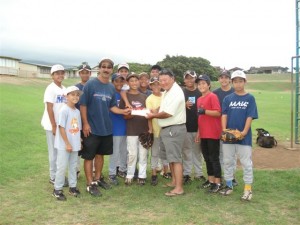 (Former Mayor Alan Arakawa presents a check to the Central East Maui Little League coach, Glenn Yonashiro on Wednesday. Courtesy Photo.)