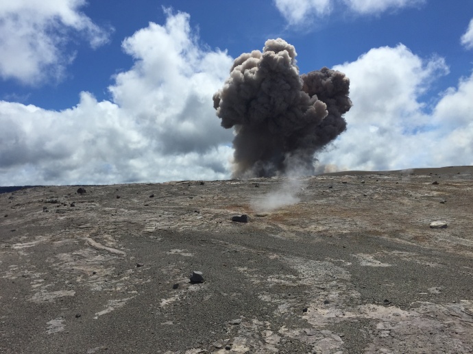 A rockfall from the wall of Halemaʻumaʻu Crater impacted the lava lake around 10:20 am, triggering an explosion of spatter and smaller particles. HVO geologists working on the far side of the crater captured the initial moments of the plume rising. The explosion deposited a large amount of spatter around the closed Halemaʻumaʻu visitor overlook. Photo courtesy USGS/ Hawaiian Volcano Observatory.