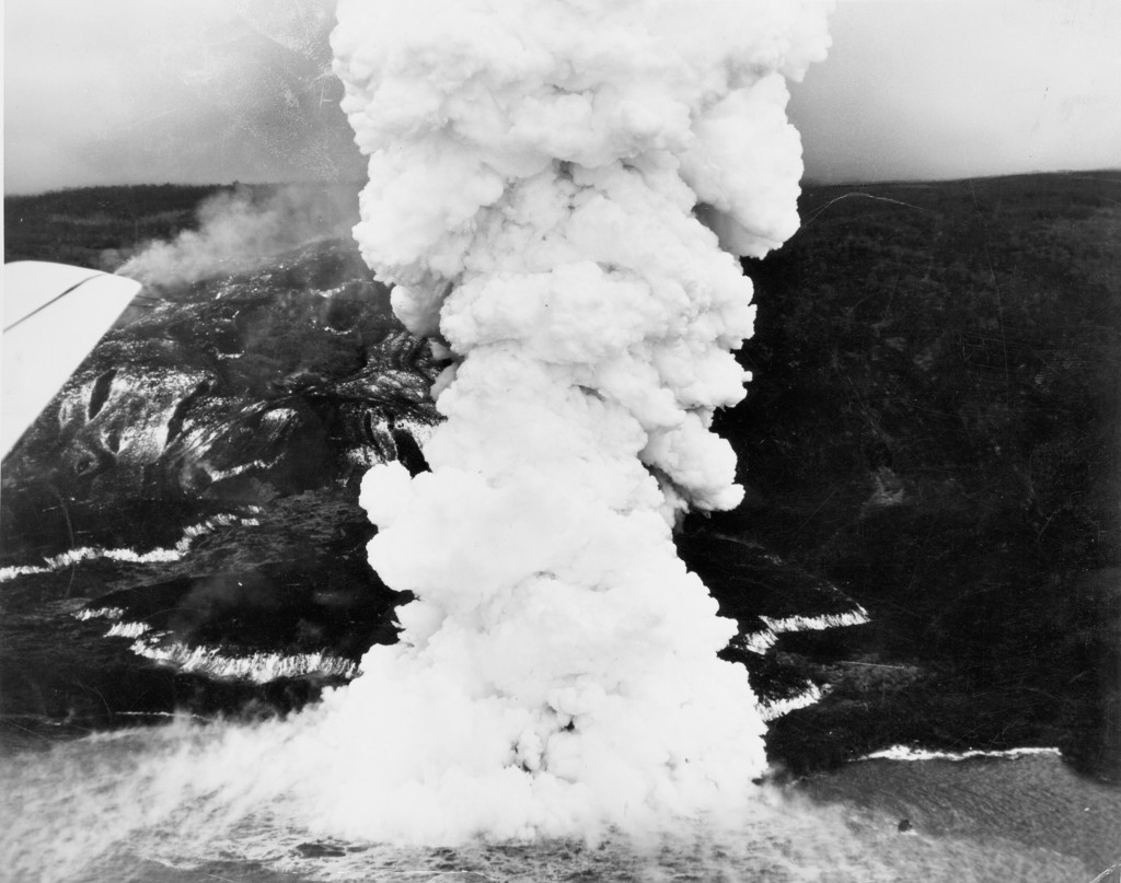 During the Mauna Loa 1950 eruption, three large, fast-moving lava flows advanced down the west flank of the volcano, each crossing the main highway before reaching the ocean. The Ka‘apuna flow, shown here, traveled from the Southwest Rift Zone vent (7,800 ft elevation) to the coast in just 17 hours, creating a huge steam plume as lava flowed into the sea. The glowing edges and fast-moving channels of the 10- to 25-ft thick ‘a‘ā flow appear white in this June 2, 1950, aerial image. Photo courtesy of Air National Guard, 199th Fighter Squadron.