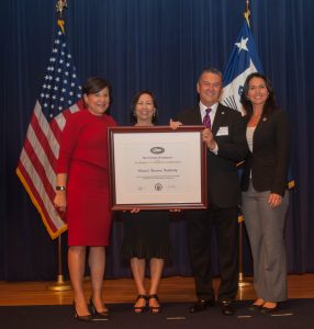 US Secretary of Commerce Penny Pritzker (left) and US Rep. Tulsi Gabbard presented the Hawai‘i Tourism Authority with the President’s “E” Award today in Washington, DC. Accepting the award was HTA President and CEO George D. Szigeti and HTA Director of Communications Charlene Chan. Photo credit: US Department of Commerce