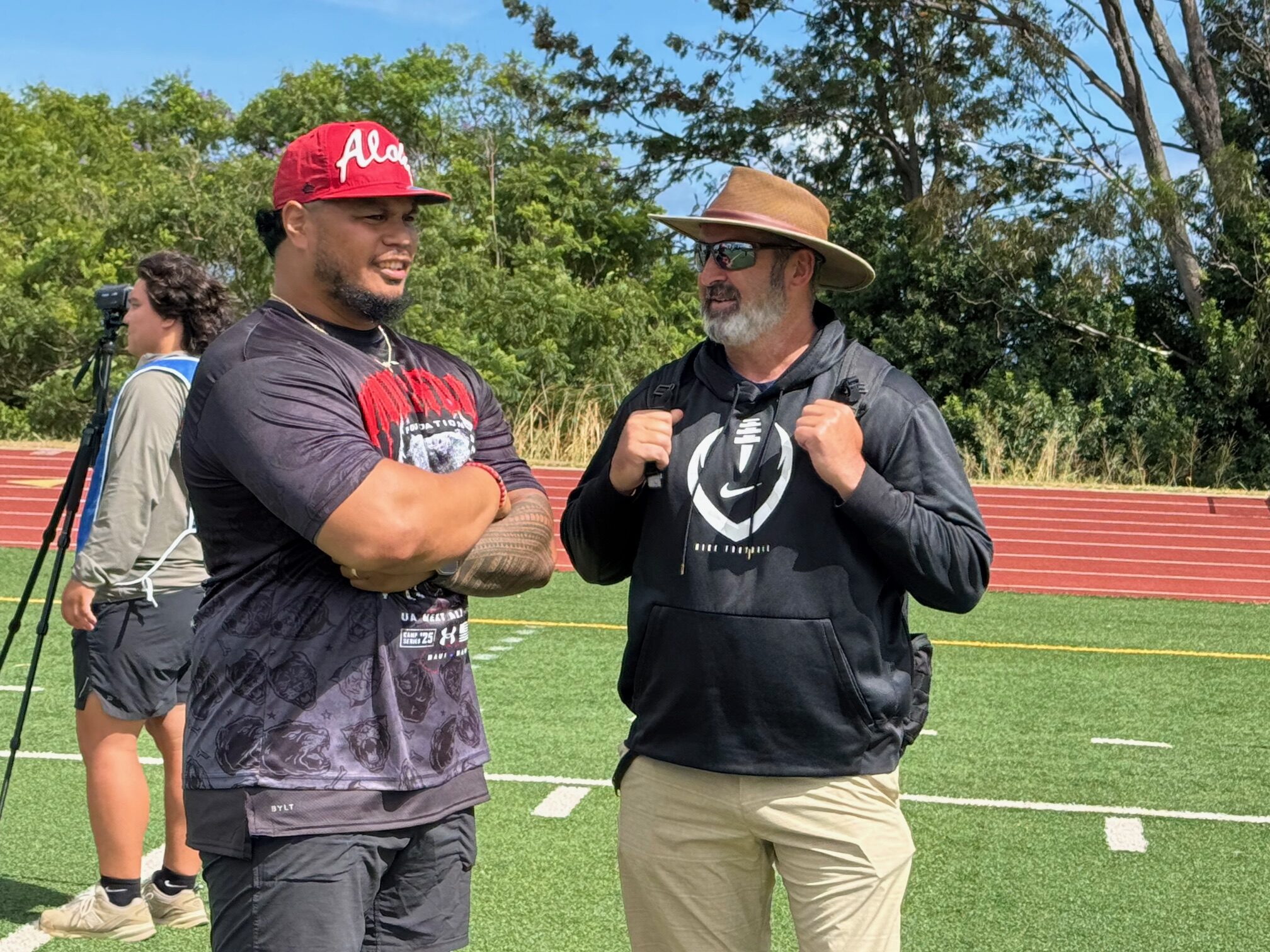 Tyson Alualu (left), a 13-year NFL defensive lineman, speaks with Cal assistant coach Nick Rolovich on Saturday at King Kekaulike Stadium during the Under Armour Next Camp. HJI / ROB COLLIAS photo