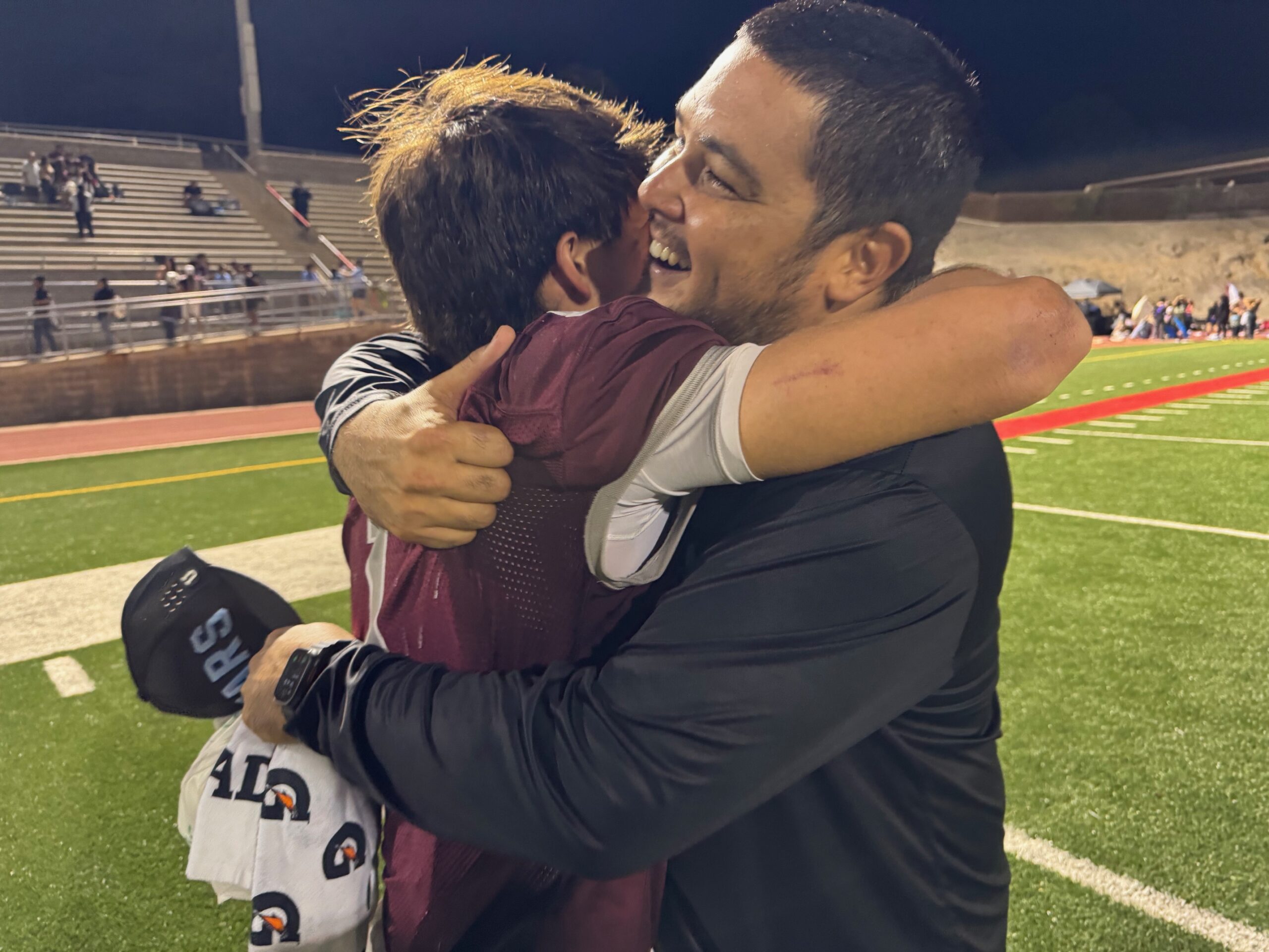 Baldwin High School coach Cody Nakamura (right) hugs quarterback Jorden Carbonell after the Bears clinched their first state tournament berth since 2019 with a 14-7 win over Lahainaluna. HJI / ROB COLLIAS photo