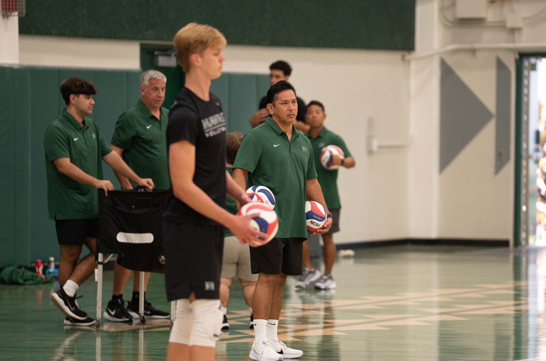 Donan Cruz, a 2001 Baldwin High School graduate (green shirt, foreground), works his first University of Hawai'i men's volleyball at practice on Sept. 29. Cruz is an assistant coach for the Rainbow Warriors. Head coach Charlie Wade (gray hair) watches on from behind the action to the left of Cruz. University of Hawai'i athletics photo